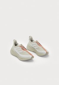 White athletic shoes with a textured upper, featuring three diagonal stripes, orange laces, and a cushioned, curved sole design.