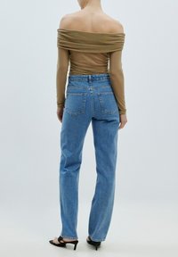 Braunfarbige, schulterfreie Langarmbluse mit Raffung, kombiniert mit hellblauen, hochgeschnittenen Jeans und schwarzen High Heels Sandalen.