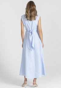 Jasnoniebieska lniana sukienka z wiązaniem z tyłu. Bez rękawów, z długością do kostek oraz gładką fakturą. Podkreślona miękką, zwiewną sylwetką.