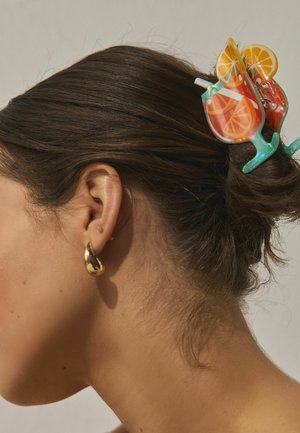 Brown hair tied up with a colorful clip shaped like an orange drink, and a gold teardrop earring visible on the left ear.