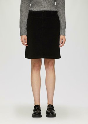 Zwarte corduroy rok met een rechte snit en subtiele voorzakken, gecombineerd met een grijze gebreide trui en zwarte lakleren schoenen.