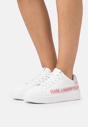 Witte lage sneakers met roze "Karl Lagerfeld"-branding en hieltab, gedragen op blote voeten tegen een eenvoudige lichte achtergrond.