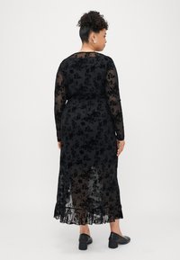 Juoda gėlėta nėriniuota suknelė su ilgomis rankovėmis, aptrauktu liemeniu ir volaniniu apvadu. Permatoma medžiaga su sudėtingomis gėlių raštais visoje suknelėje.