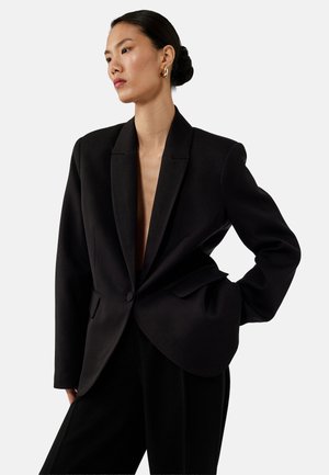 Zwarte op maat gemaakte blazer met een diepe V-hals, enkele knoopsluiting, gestructureerde schouders en zijzakken, gemaakt van een gladde stof.