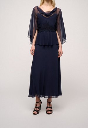 Navyblauwe jurk met doorschijnende, flonkerende mouwen, kantdetail bij de taille en een vloeiende rok. Gepaard met zwarte bandjeshakken.