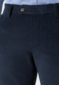 Ciemnoniebieskie spodnie sztruksowe z teksturowanej tkaniny, o prostym kroju i zapinane na jeden guzik. Widoczne detaliczne przeszycia na szwach.