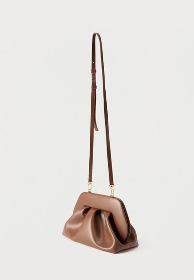 Καφέ δερμάτινη τσάντα ώμου με σχεδιασμό με πιέτες και ρυθμιζόμενο λουρί, εμφανίζεται κρεμασμένη σε λευκό, απλό φόντο.