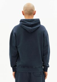 Marineblauwe sweatshirt met een capuchon, losse pasvorm, geribde boorden en zoom, zachte textuur, en een klein logo op de achterkant.
