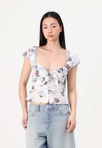 Top corto floreale con maniche corte a volant; tessuto bianco con motivi floreali blu e marroni; dettaglio frontale annodato; orlo a peplo.