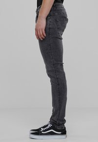 Uske slim-fit, sivi traperice s izblijedjelom teksturom. Ima pet džepova, zatvaranje na zip i petlje za remen. Uparene s crno-bijelim tenisicama na vezanje.