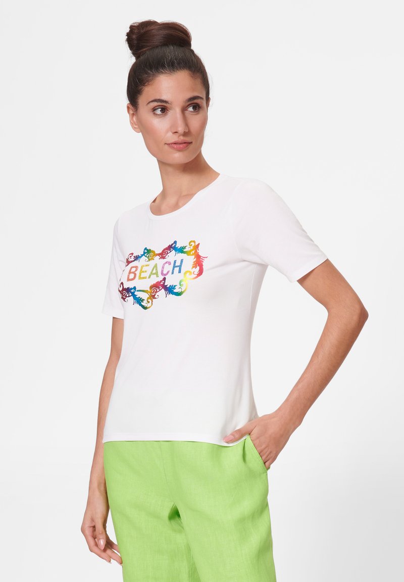 White short-sleeve t-shirt featuring a colorful "BEACH" graphic surrounded by intricate designs. Material is soft and smooth.