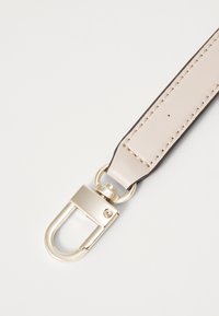 Cinturino in pelle beige con cuciture scure e un gancio in metallo dorato. Il cinturino ha una superficie liscia ed è di forma rettangolare.