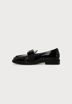 Mocassin en cuir verni noir avec petit talon, nœud gros-grain noir décoratif et clous argentés sur le dessus, présenté de profil sur fond blanc.
