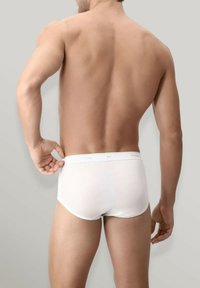 Mutande bianche in cotone con elastico in vita, design aderente e texture liscia, viste da dietro su uno sfondo neutro.
