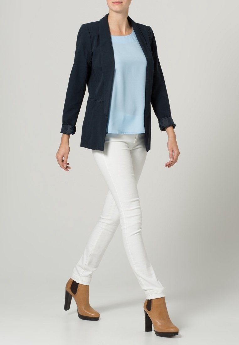 Marinblå blazer, ljusblå topp, vita skinny jeans och bruna ankelstövlar med svarta klackar. Blazern har en skräddarsydd design och uppvikta ärmar.