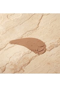 Brown cream product smeared in a smooth curve on a light beige textured surface, resembling stone with subtle veining.