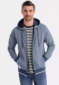 Sweat à capuche zippé en bleu chiné avec des accents marine, doté d'une poche frontale, de cordons de serrage ajustables et de poignets à côtes.