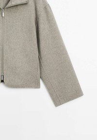 Szara marynarka z wełny z krótkim krojem, z wysokim kołnierzem i zapięciem na zamek. Teksturowany materiał, szerokie rękawy i proste linie.