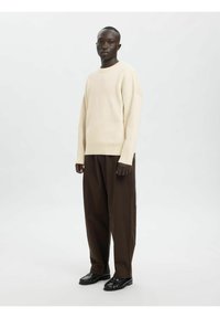 Kremni rebrasti pulover, sproščen kroj; temno rjave široke hlače; črni čevlji. Preprost dizajn z rahlo spuščenimi rokavi na ramenih.