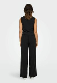 Combinaison noire sans manches avec un haut ajusté et un pantalon à jambes larges, fabriquée dans un tissu lisse. Présente un design simple sans motifs visibles.