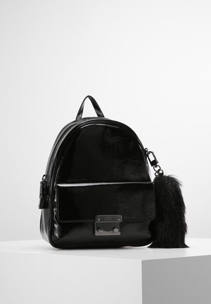 Mini sac à dos noir brillant avec poche avant, fermoir métallique, poignée supérieure et grand porte-clés noir duveteux attaché à la fermeture éclair.