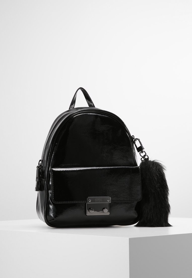 Mini sac à dos noir brillant avec poche avant, fermoir métallique, poignée supérieure et grand porte-clés noir duveteux attaché à la fermeture éclair.