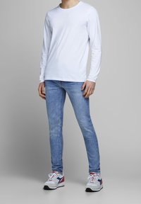Camiseta blanca de manga larga, jeans ajustados de color azul claro y zapatillas multicolores con detalles en rojo, azul y gris. Diseño sencillo y estilo casual.