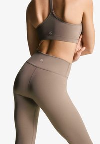 Brun sport crop top og high-waisted leggings lavet af glat, strækbart stof med tonale syninger og et lille logo på elastikken.