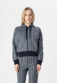 Námornícka zipsová mikina so zodpovedajúcimi nohavicami. Obsahuje geometrický vzor, ribbované rukávy a kapucňu so šnúrkou.
