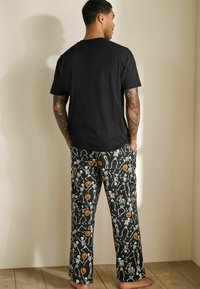Sort kortærmet t-shirt parret med sorte pyjamabukser med orange græskar og hvide skeletter på en sort baggrund.