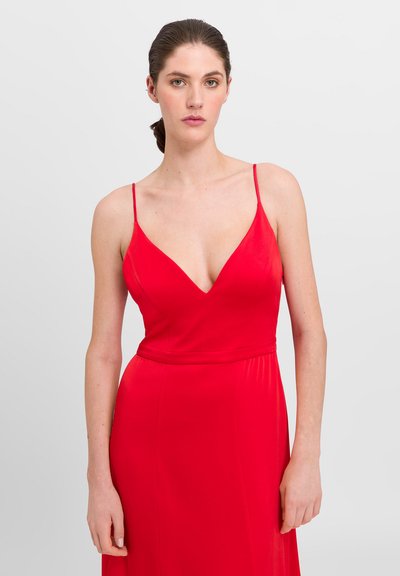Red sleeveless dress with a deep V-neckline, made of smooth fabric. Features thin shoulder straps and a fitted waist, flowing skirt.