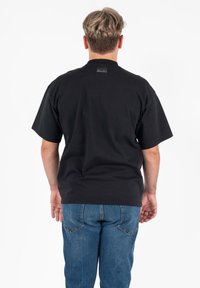 Zwarte korte mouwen T-shirt met een ronde hals en een rechthoekig merklabel aan de achterkant; gecombineerd met blauwe denim jeans, gladde textuur.