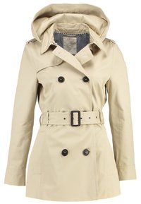 Trench-coat beige à double boutonnage avec boutons noirs, taille ceinturée, large col et capuche fixée.