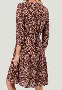 Robe à imprimé léopard avec des manches trois quarts, taille cintrée et ourlet en couches. Tissu doux dans des teintes beige, marron et noir.