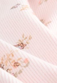 Tessuto rosa tenue a coste con motivo floreale in marrone chiaro, rosa e verde, dalla texture leggermente sfocata e pieghe stratificate.