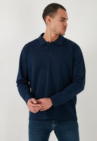 Polo de manga larga color navy con una tapeta de tres botones y cuello. Textura suave y corte relajado, combinado con pantalones de mezclilla.