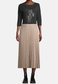 Top negro de manga tres cuartos con letras gráficas en gris; falda midi plisada color crema con patrón de cuadros; botas negras hasta el tobillo con acabado texturizado.