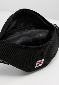 Custodia in rete nera con zip e patch del logo Fila, parzialmente aperta che mostra l'interno vuoto.