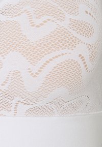 Witte beha met een gestructureerde kanten bovenrand met een zigzagpatroon en een gladde, effen witte onderband. Lichtgewicht, doorschijnend ontwerp.