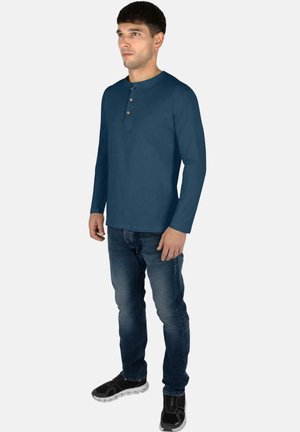 Long-sleeve navy shirt with a henley neckline featuring three wooden buttons, paired with blue jeans and black athletic shoes.