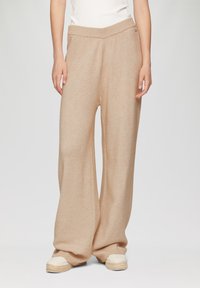 Beige wijde broek met een zachte textuur, geribde tailleband en een relaxte pasvorm, gecombineerd met lichte espadrilles.