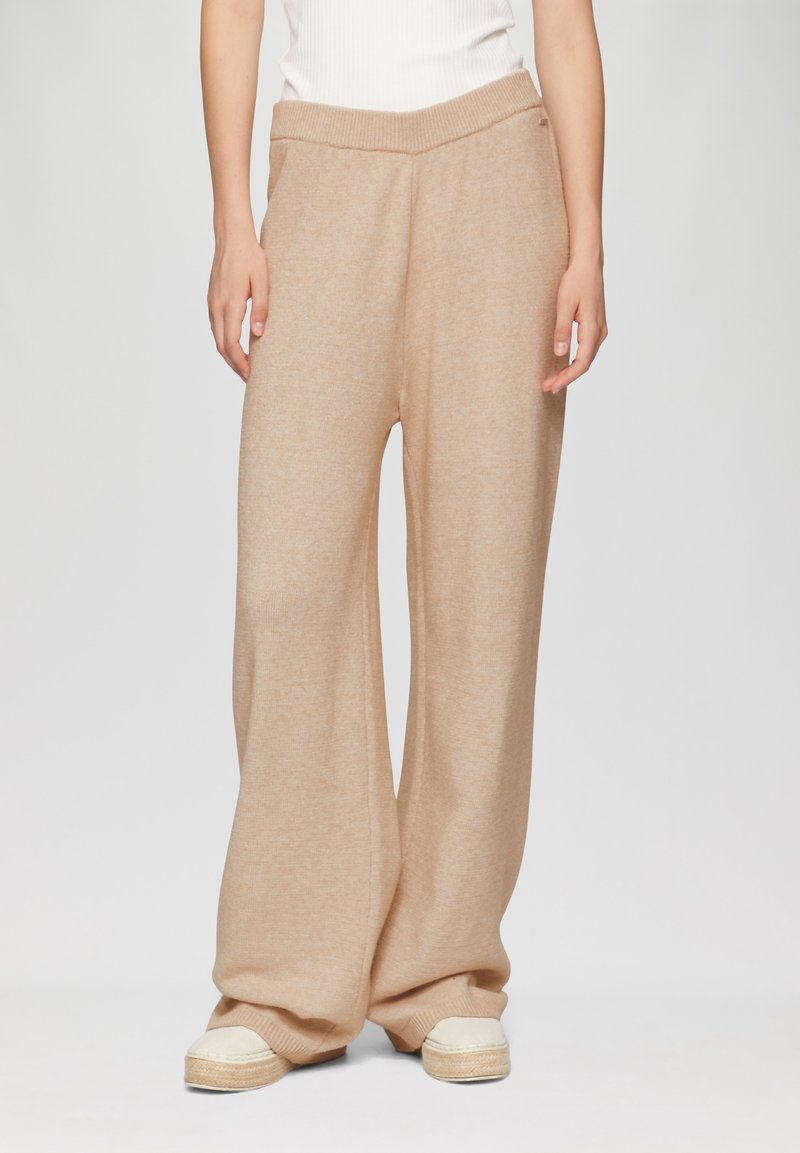 Beige wijde broek met een zachte textuur, geribde tailleband en een relaxte pasvorm, gecombineerd met lichte espadrilles.