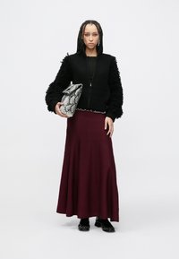 Černá žebrovaná bunda na zip s texturovanými rukávy, bordó sukně a metallická kabelka se vzorem hada. Černé boty s texturovanými detaily.