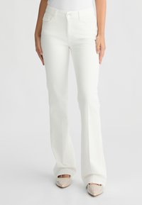 Jeans bianchi a zampa d'elefante realizzati in tessuto misto cotone, con tasche frontali, chiusura a bottone e una texture liscia. Indossati con ballerine impreziosite.
