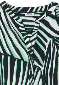 Blouse à col avec motif rayé abstrait en noir, blanc et vert menthe, et trois boutons noirs sur la patte de devant.