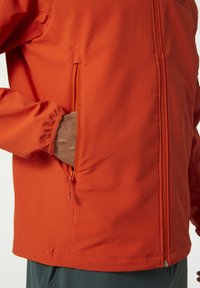 Chaqueta softshell naranja con un bolsillo con cremallera en el costado, tejido texturizado, corte relajado y puños ajustables para mayor comodidad.
