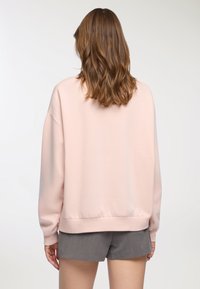 Jasnoróżowy sweter z luźnym krojem, opadającymi ramionami i ściągaczami. Miękka tkanina o gładkiej fakturze, zestawiona z szarymi szortami.