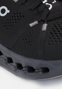 Schwarzer Sportschuh mit einem atmungsaktiven Obermaterial aus Netzstoff, grauen Akzenten und einer gepolsterten Sohle mit strukturiertem Muster.