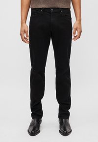 Jeans de mezclilla negra con ajuste slim, que presentan bolsillos delanteros, costuras sutiles y un cierre de botón, combinados con zapatos de vestir negros texturizados.