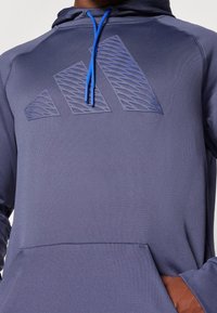 Felpa con cappuccio blu navy con logo testurizzato in tono. Presenta lacci blu a contrasto e una tasca frontale. Tessuto dallo stile liscio.